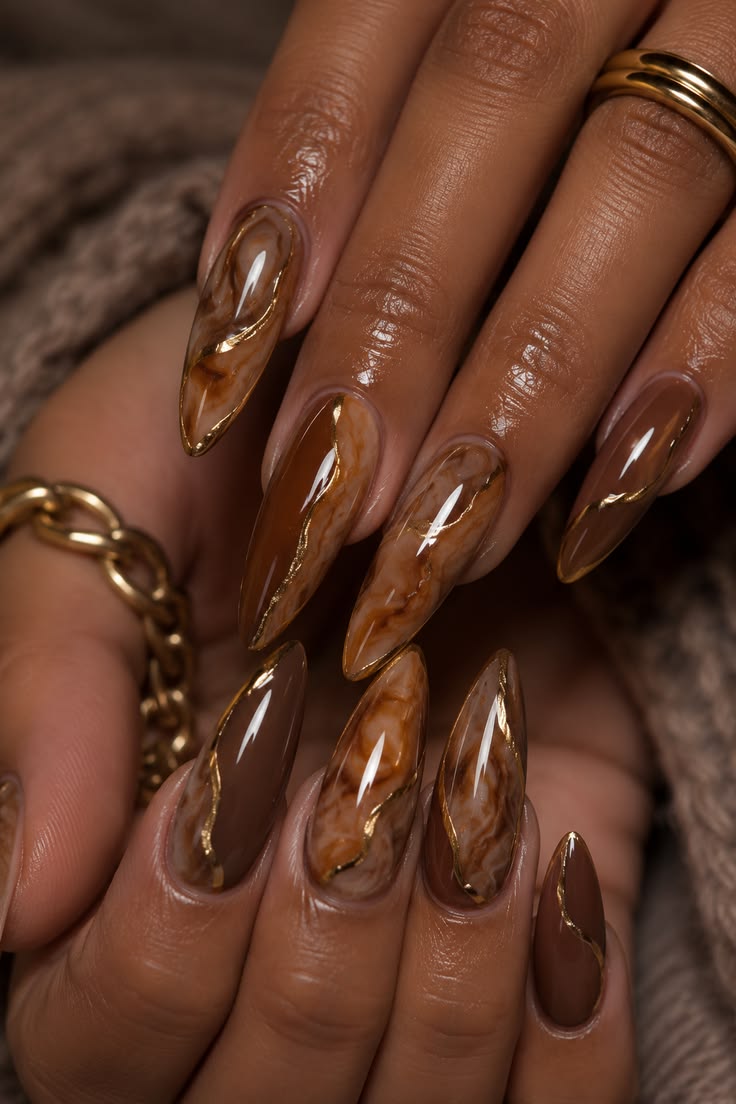 Main aux longs ongles amande bruns portant des bagues dorées